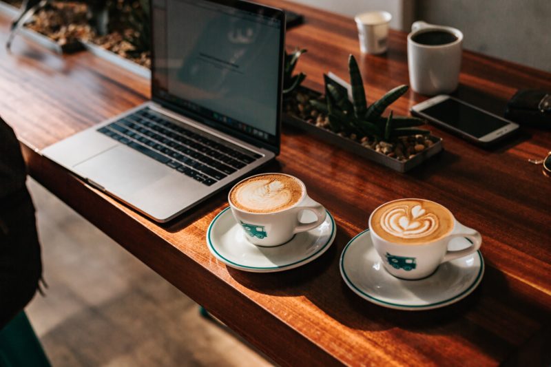 Two cappuccino served on cups near laptop computer